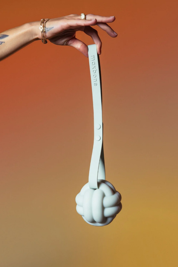 Hand holding a mint silicone knot pet toy against an orange gradient background